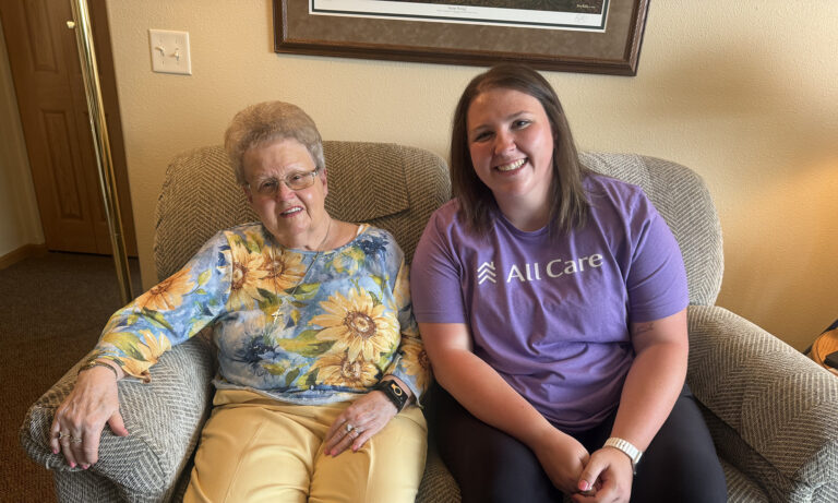Older woman and her caregiver smiling together while seated side by side.